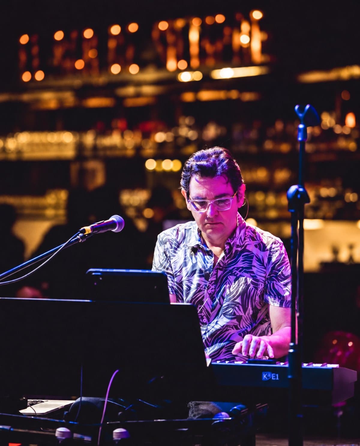 Eduardo Maya Posada al teclado en un escenario, con el bar iluminado al fondo